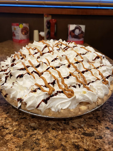An view of a pie topped with lots of cream and caramel and chocolate sauce drizzle.