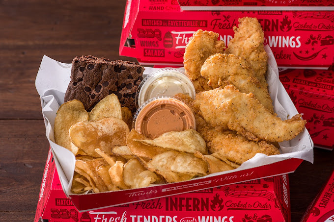 Breaded chicken, potato chips, two close sauce cups, and a chocolate chip brownie, all in a red box.