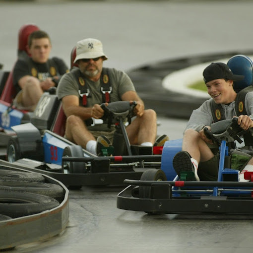Three guys riding go-karts, just about to turn the corner on the track.