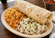 Large breakfast burrito served with Mexican-style rice, cheesy pinto beans, and a side of red salsa on a cream-colored plate.