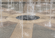 Close-up of an interactive splash pad fountain with multiple water jets rising from textured concrete paving.