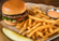 Classic cheeseburger served with golden French fries and a small cup of dipping sauce on a parchment-lined metal tray.