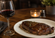Grilled steak served on a white plate beside a glass of red wine on a warmly lit restaurant table with a softly blurred background.