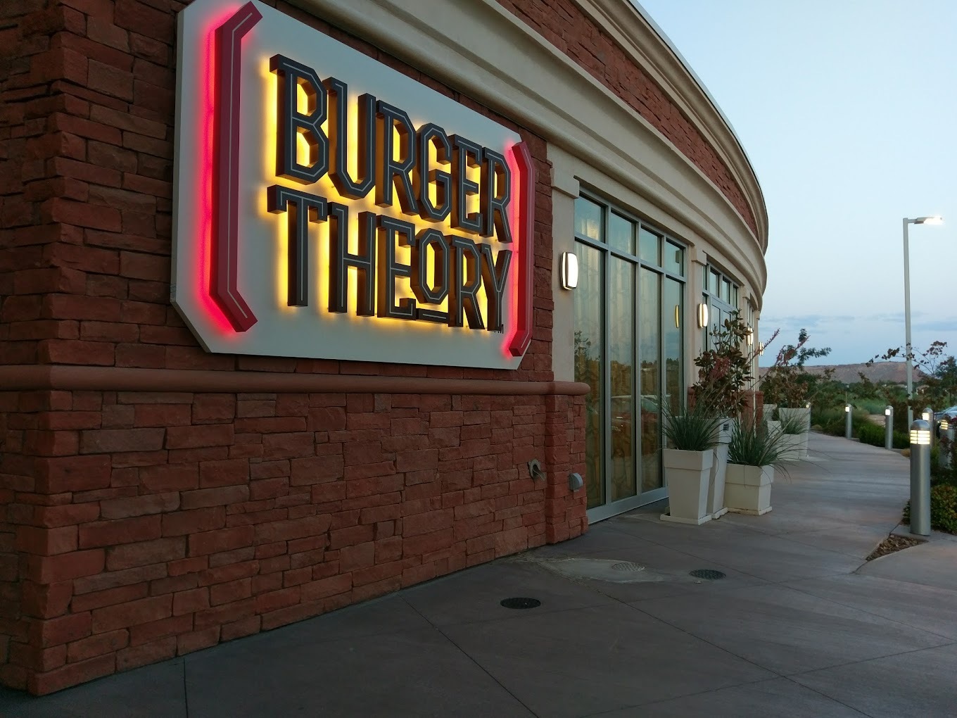 A brick building with lots of windows, a large lighted sign at eye level reads "Burger Theory"