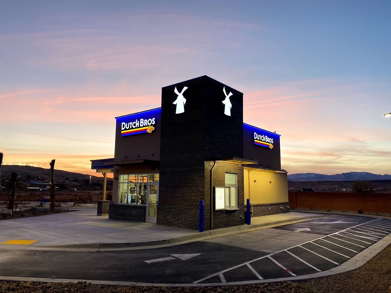 A beautiful blue and pink sunset scene in the background of a modern blue and brown colored Dutch bros building.