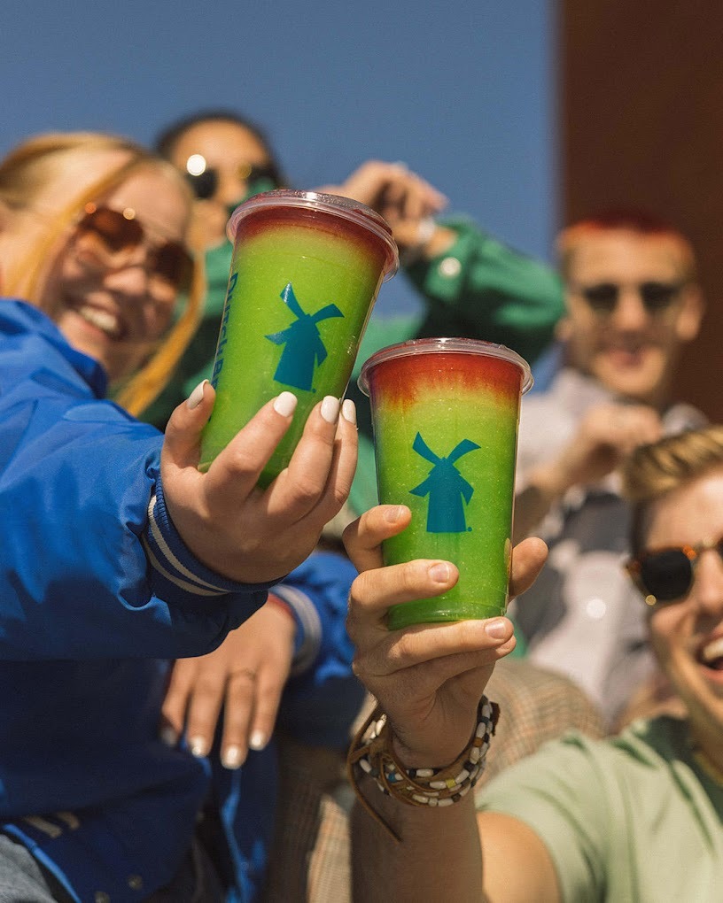 A group of people holding up their green and red specialty Dutch Bros drinks.