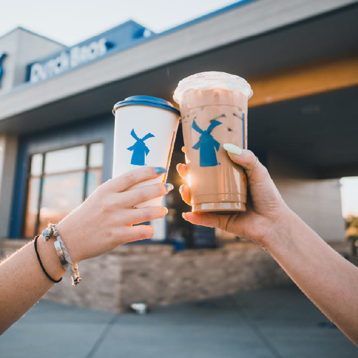 Two people holding up their large Dutch Bros iced lattes and doing a cheers with the rims of their drinks.