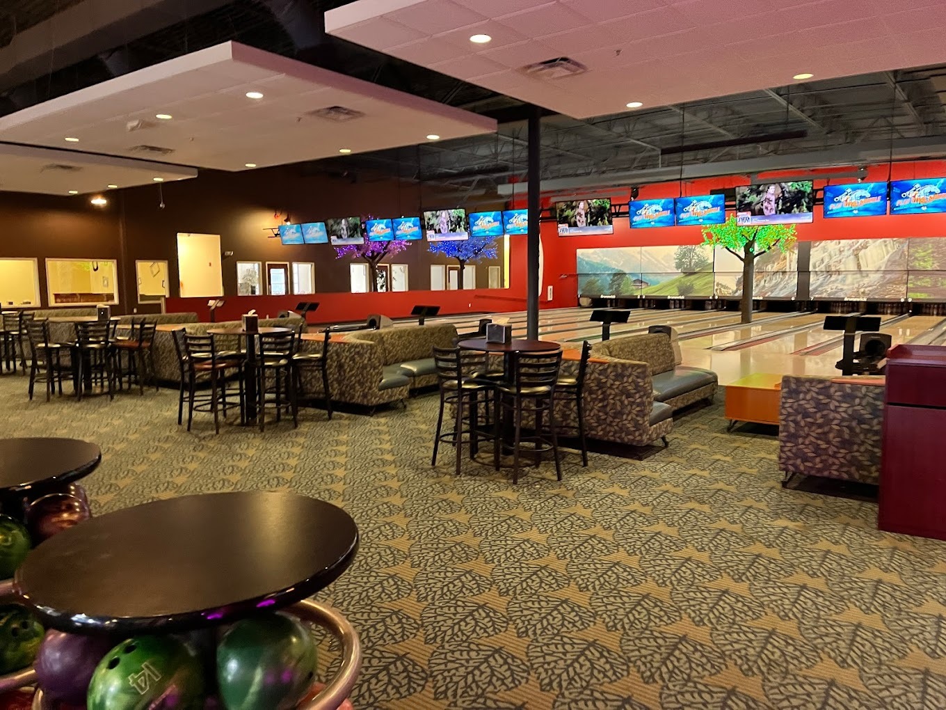 A large dining area with bowling lanes in the background, TVs line the back walls of the lanes.