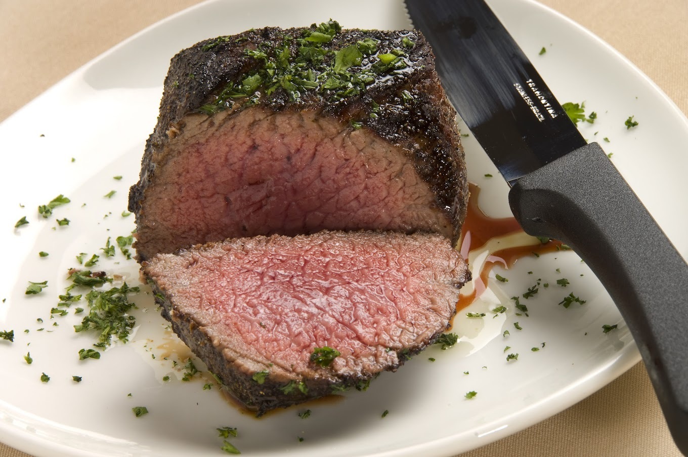 A white plate with a steak garnished with green leaves and sliced open to see the pink center.