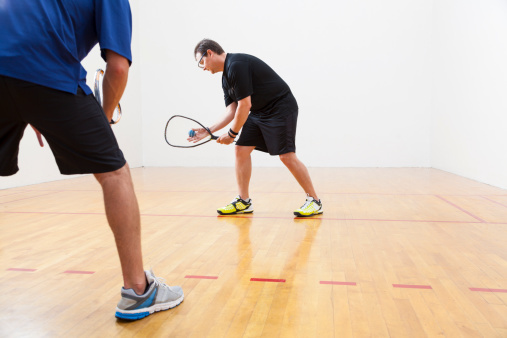 two men playing tennis in a large white room with a  court floor.