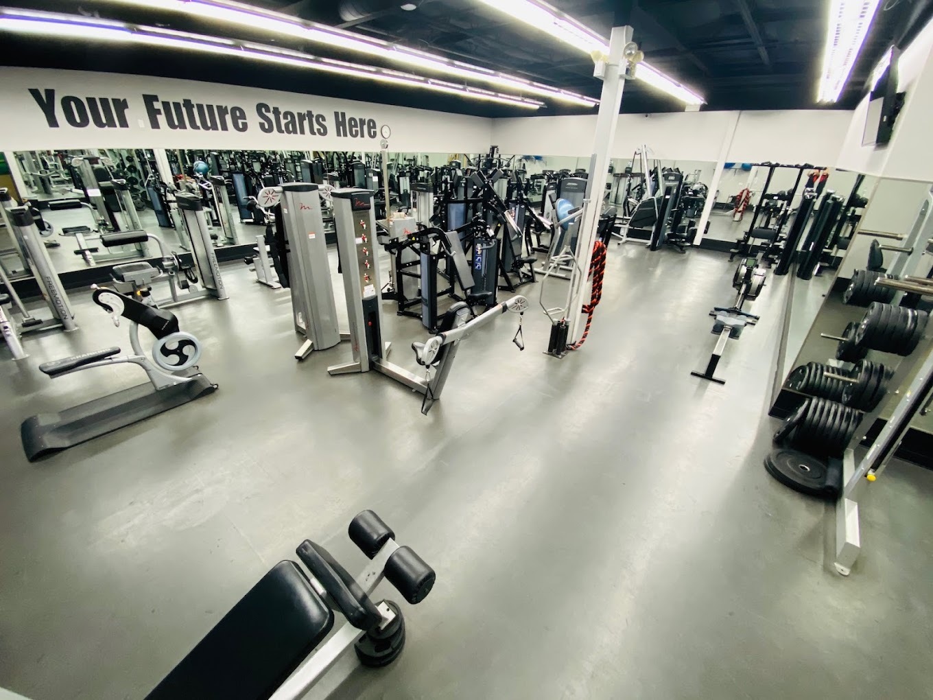 Large white room with mirrors on the wall filled with equipment for working out.