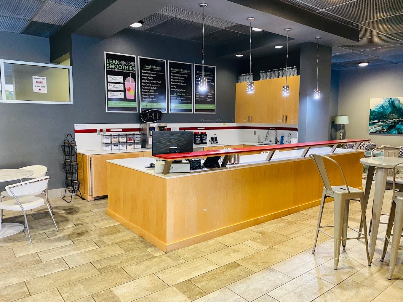 A black painted room with a front counter/bar area with a smoothie menu on the wall above the counter. Tables and chairs fill the sitting area.