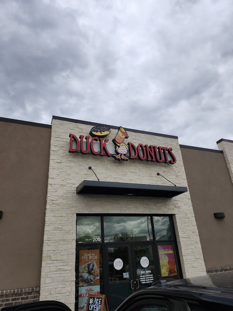 An outside view of an modern styled strip mall with an sign above the door reading "Ducks Donuts"