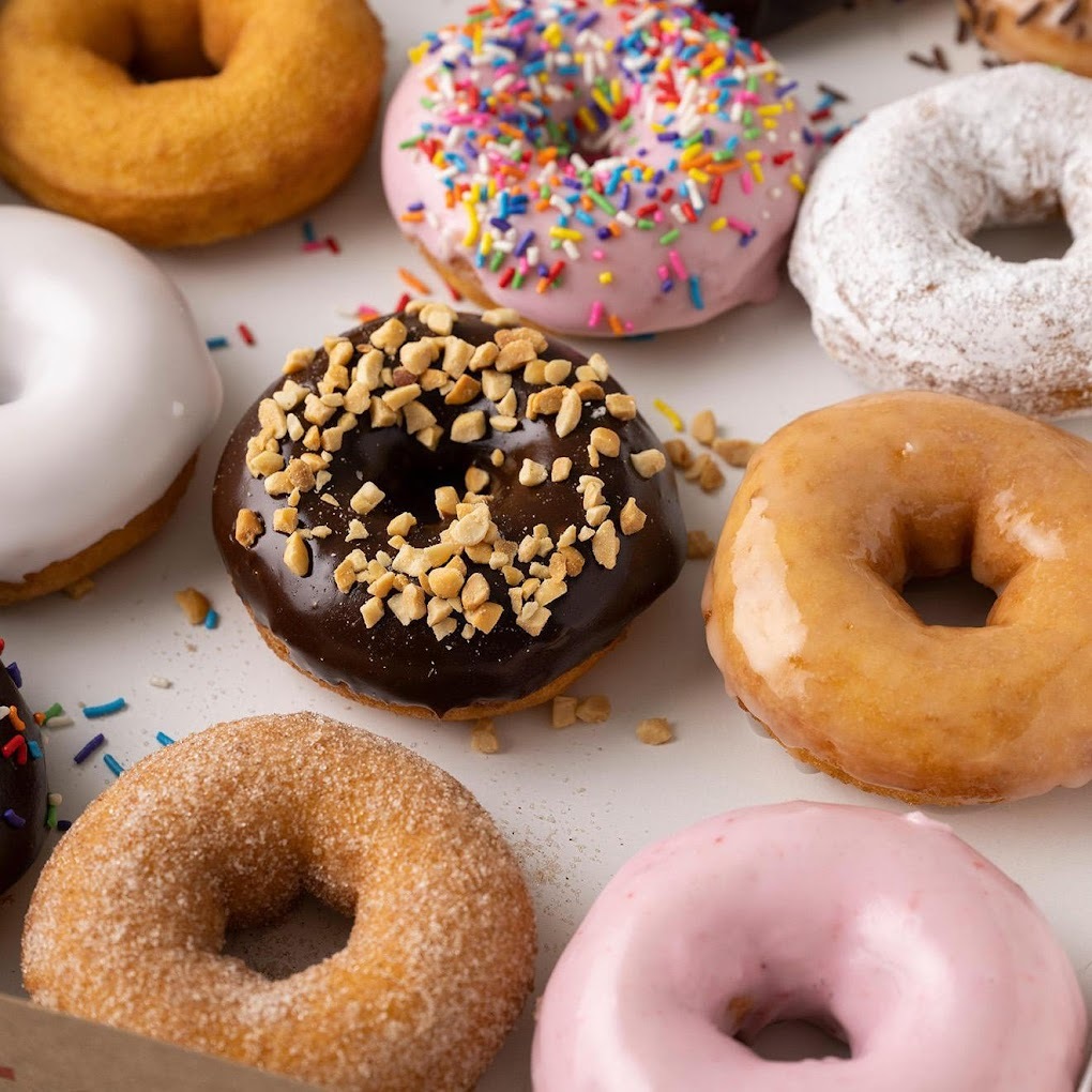 A view of donuts lined up, varying from glazed, frosted with chocolate, vanilla, or strawberry icing.