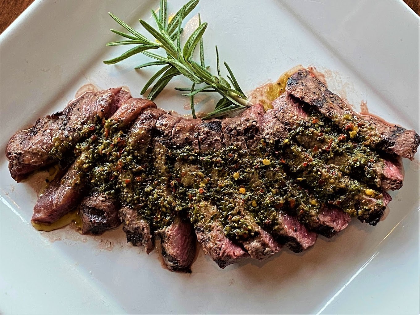A white plate with grilled steak and a green garnish