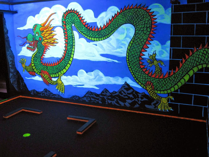 A mini golf glow course with an painting of a dragon on the wall.