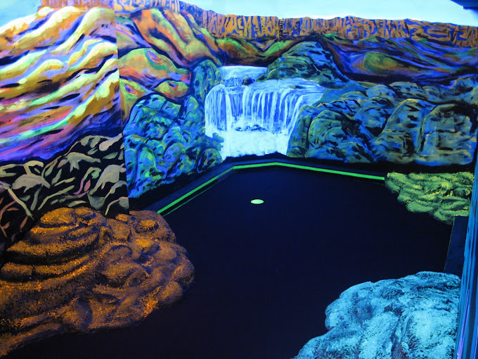 An inside view of an glow in the dark golf course, the designs in the wall resemble space and a waterfall.