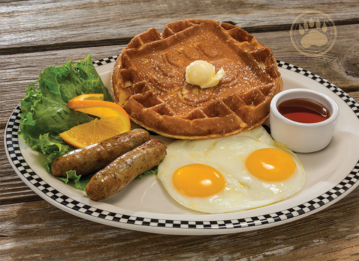 A white plate and blue detailing with a classic breakfast of waffles, eggs, lettuce, sausage and an orange.