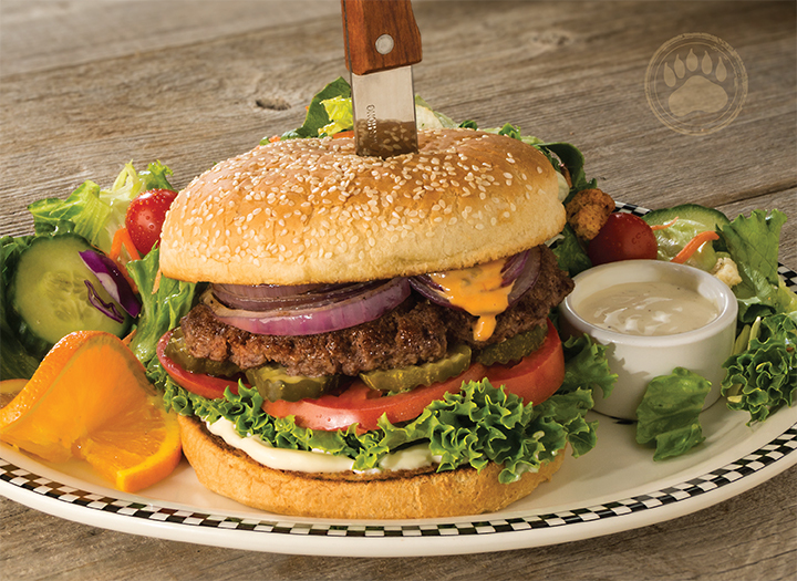 A white plate with a burger and lots of sides like pickles, ranch, and lettuce.