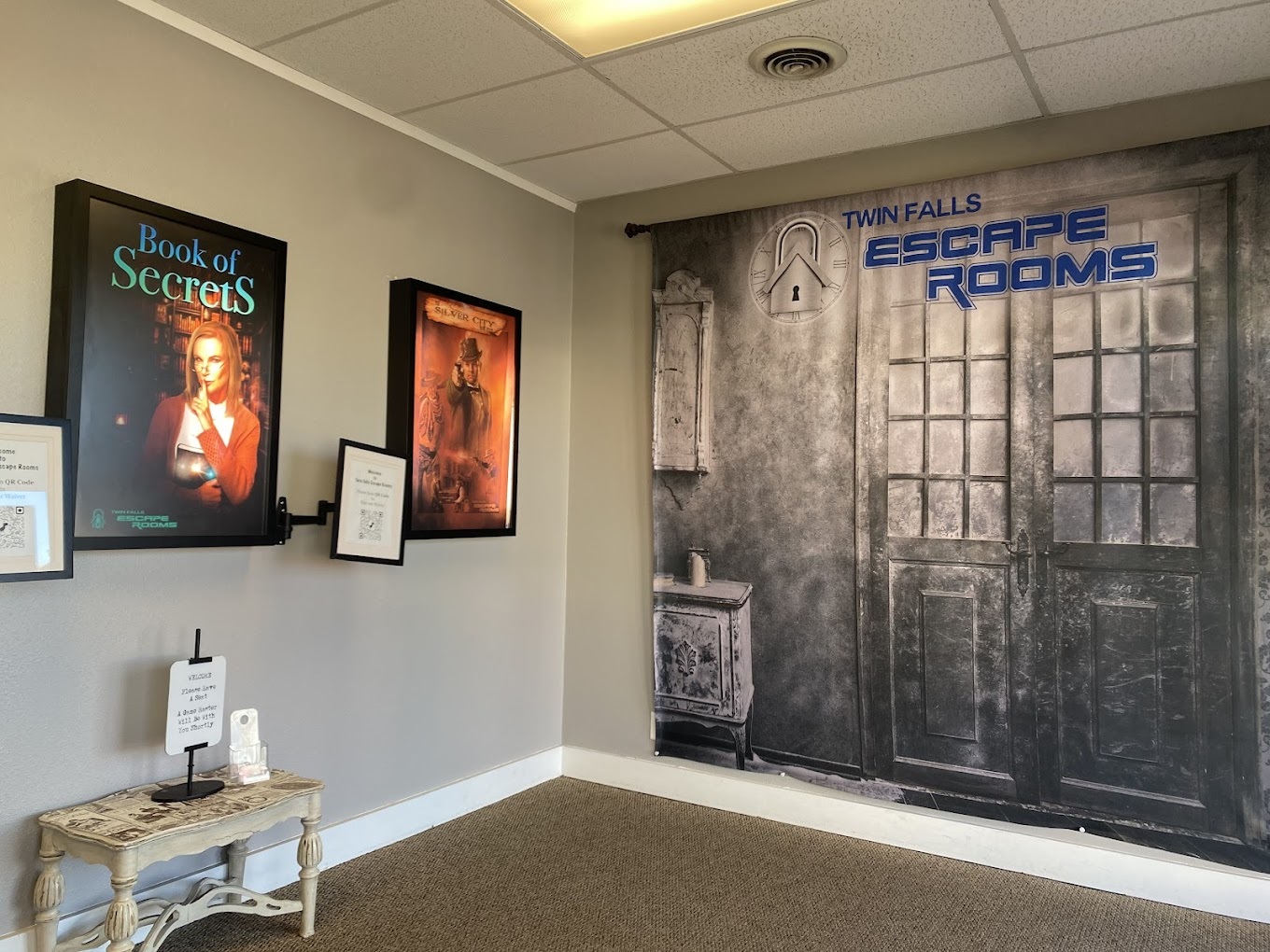An view of a lobby for an escape room, posters on the wall and a table.