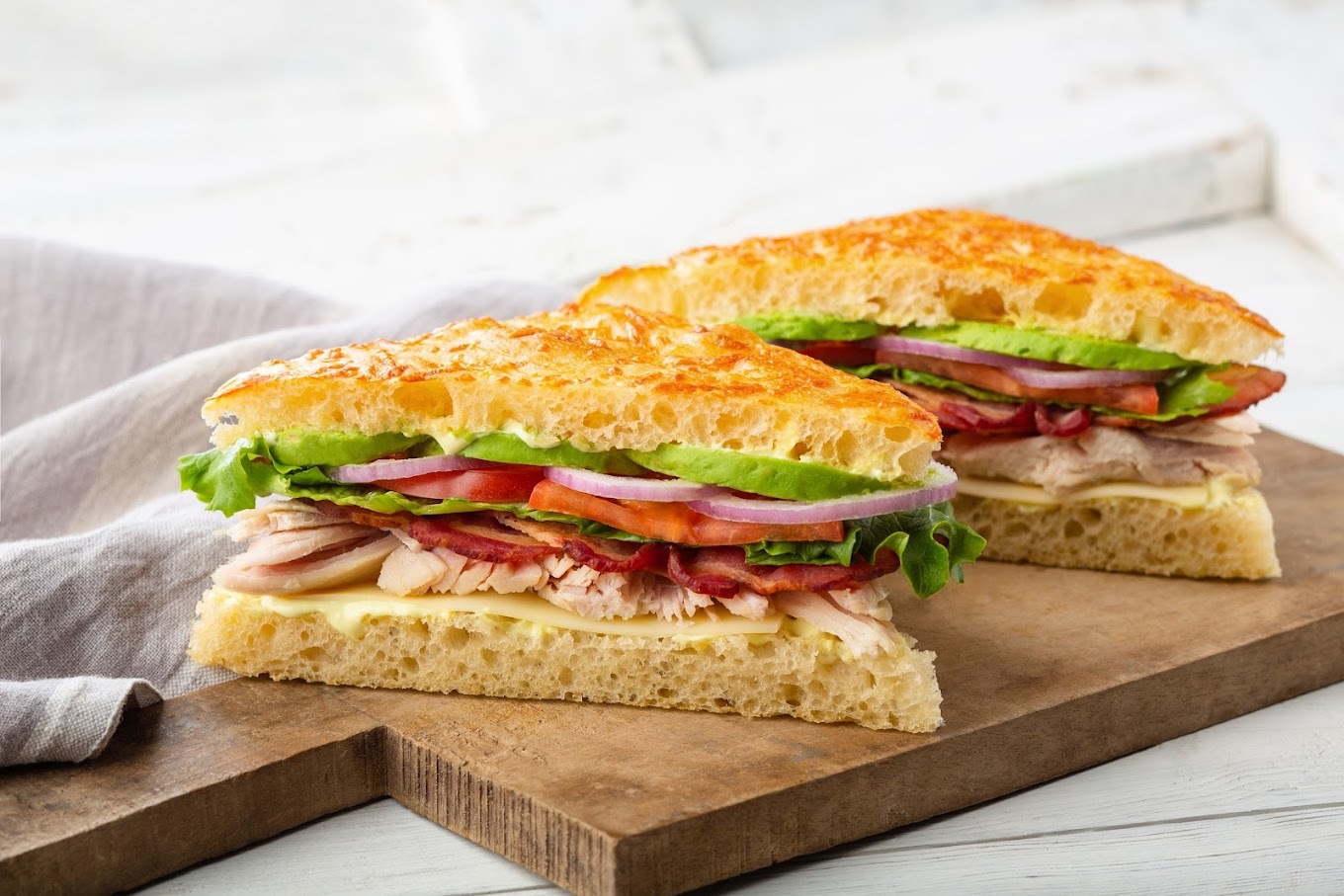 A sandwich cut in half on a cutting board, containing meat, lettuce, tomatoes and cheese.