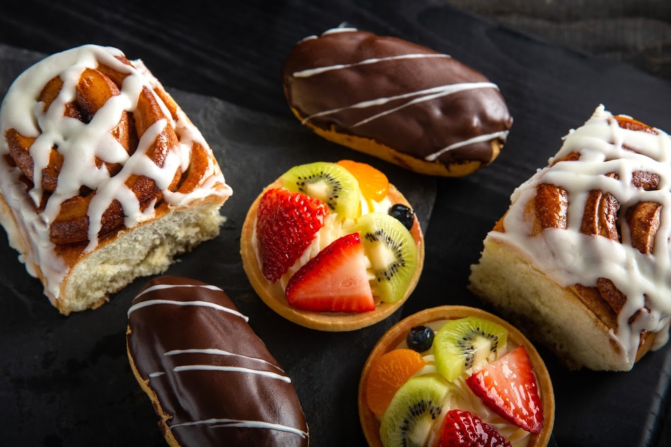 A close up image of all kinds of chocolate drizzled treats, donuts, tarts, and scones.