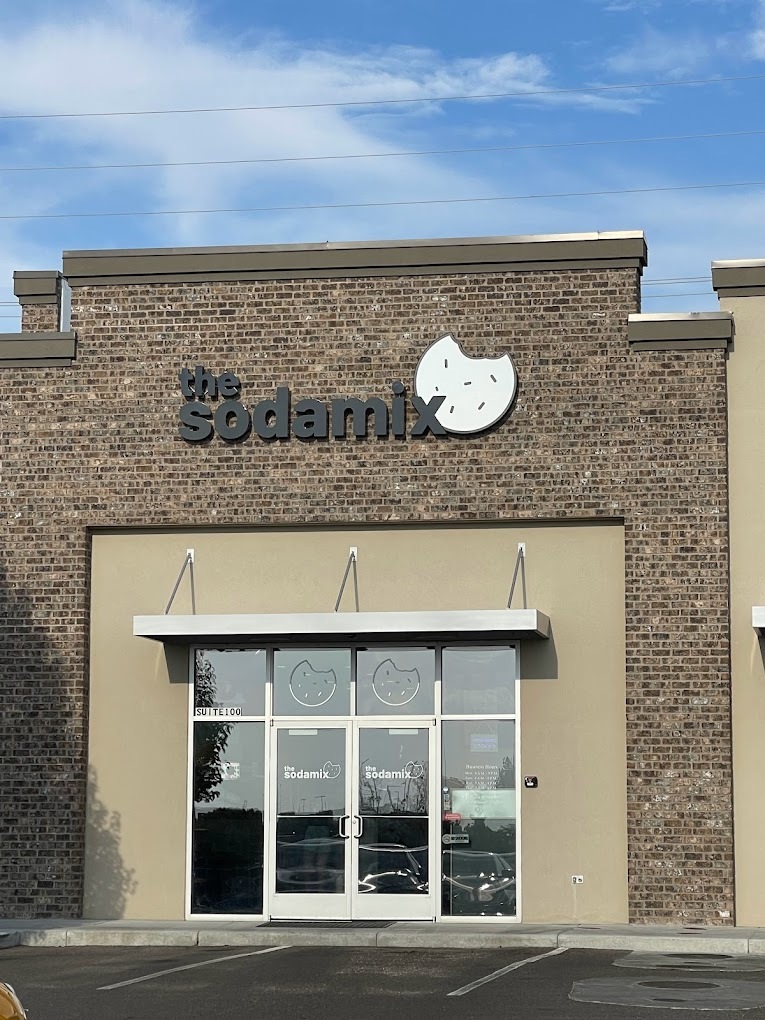 A stone and tan colored building with white windows and doors in the middle, with a large sign reading "Soda Mix" in black lettering.