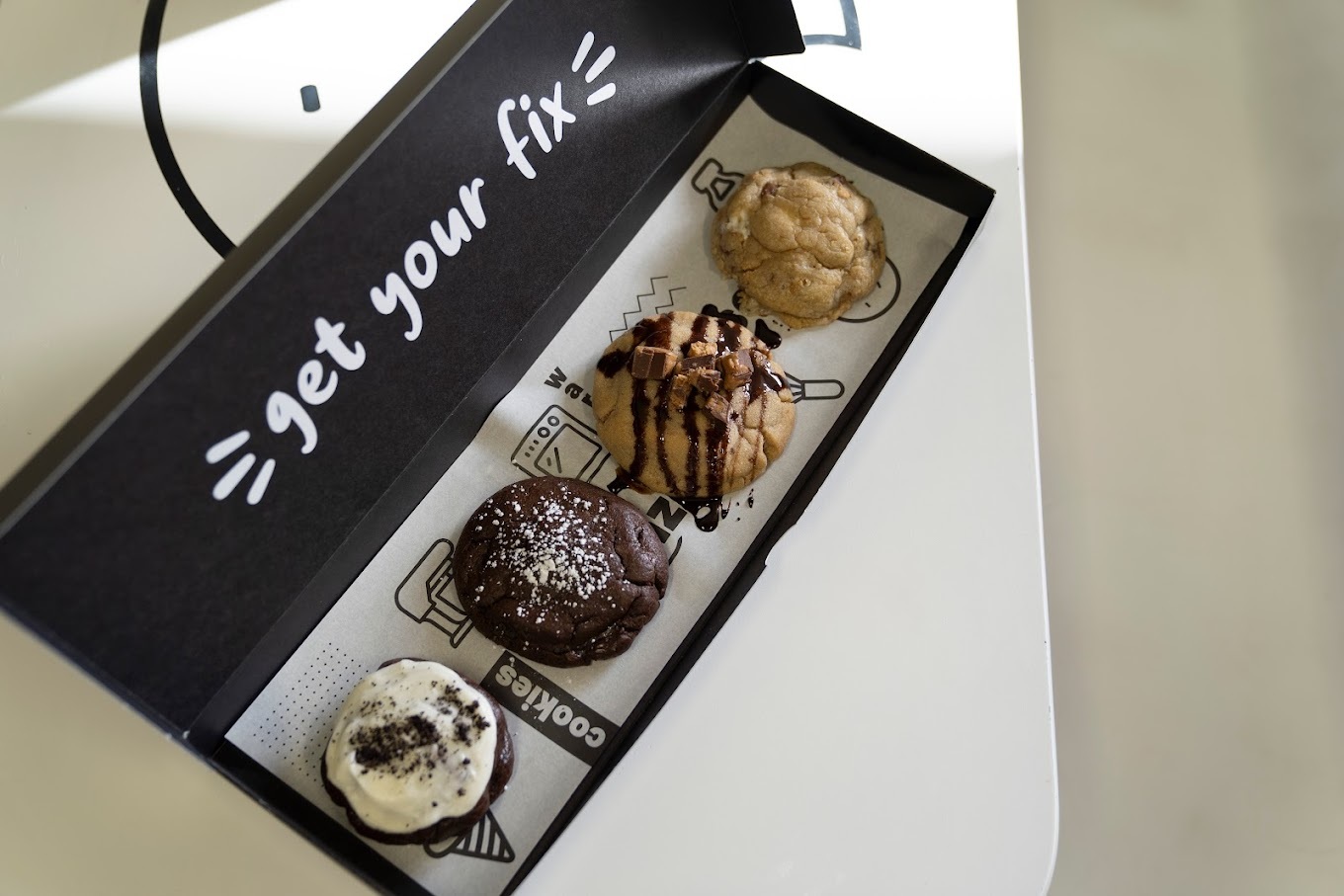 A black rectangular box of four cookies, the top of the box reads "Get your fix"