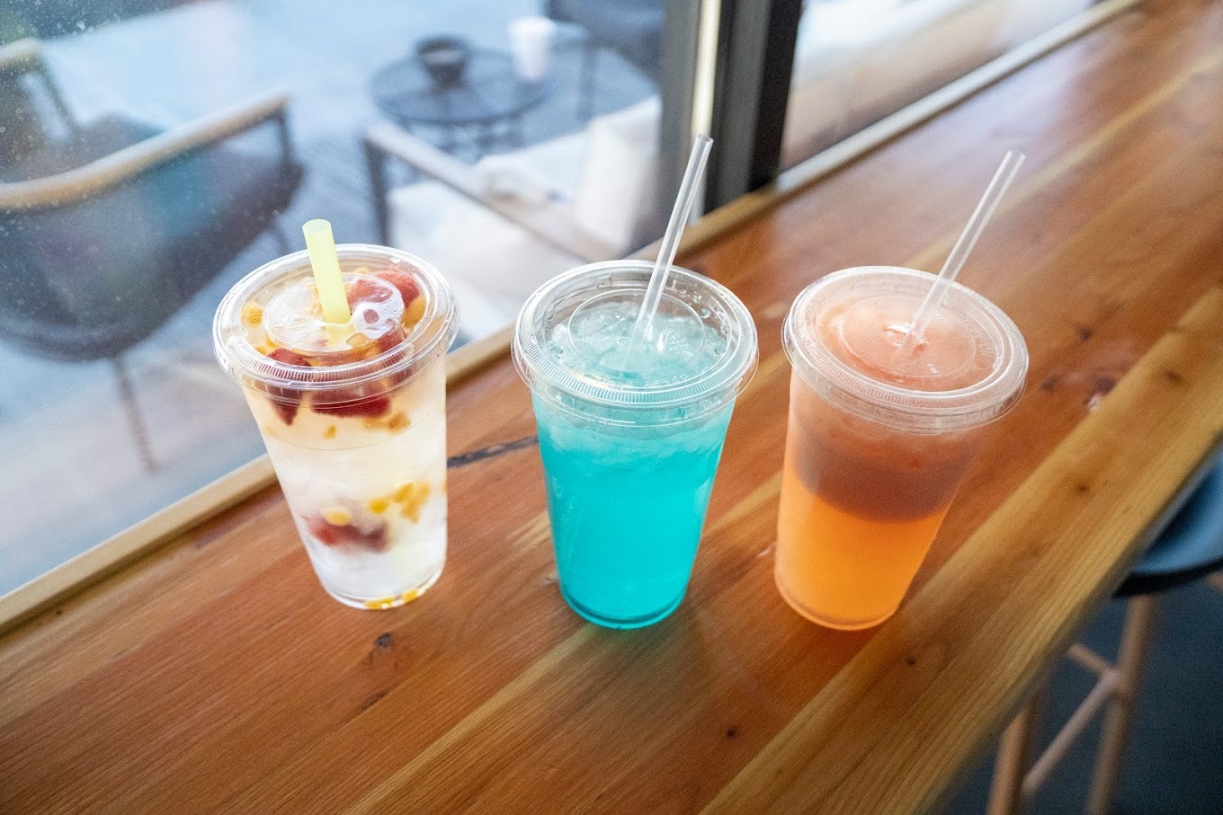 Three drinks lined up, a clear drink with fruits inside, a bright blue drink. and a orange drink.