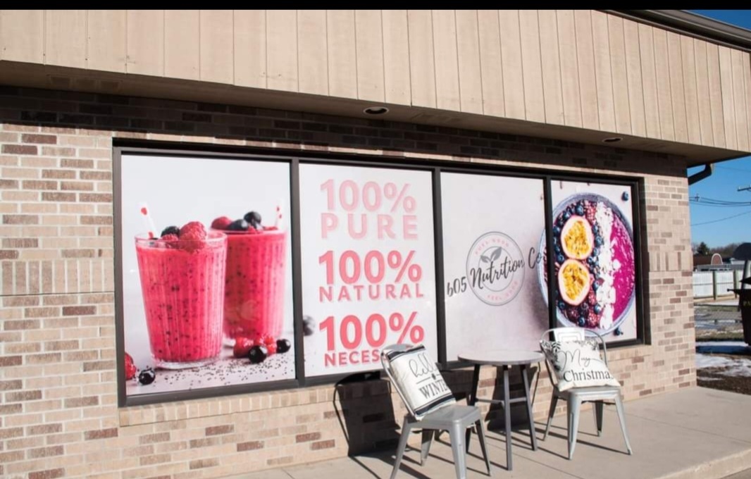 View of the entrance to a shake shop, with window decals depicting smoothies and chairs out front.