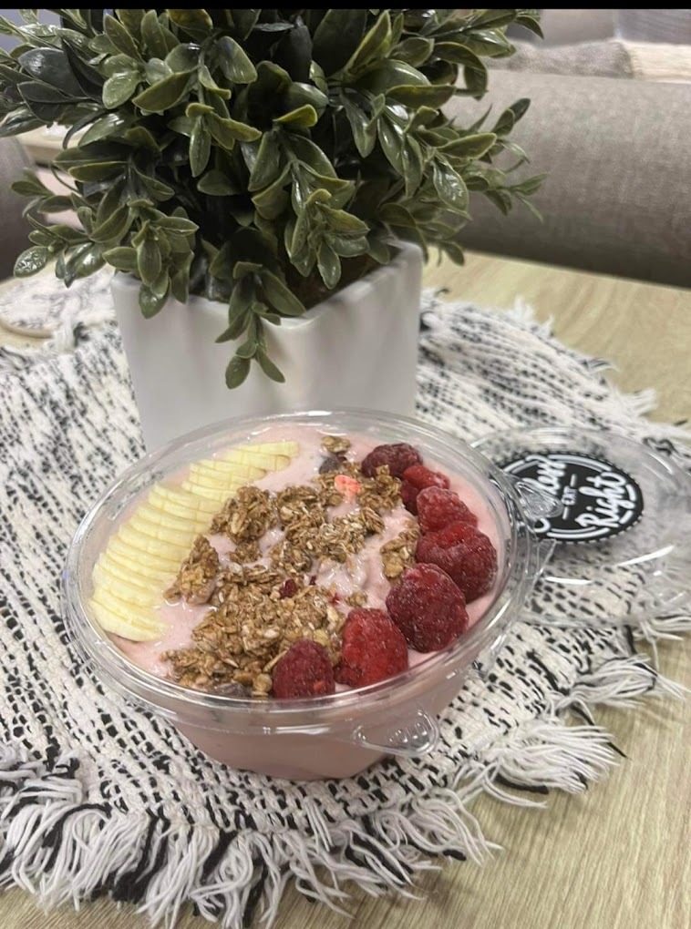 A smoothie bowl topped with raspberries, granola and sliced banana.