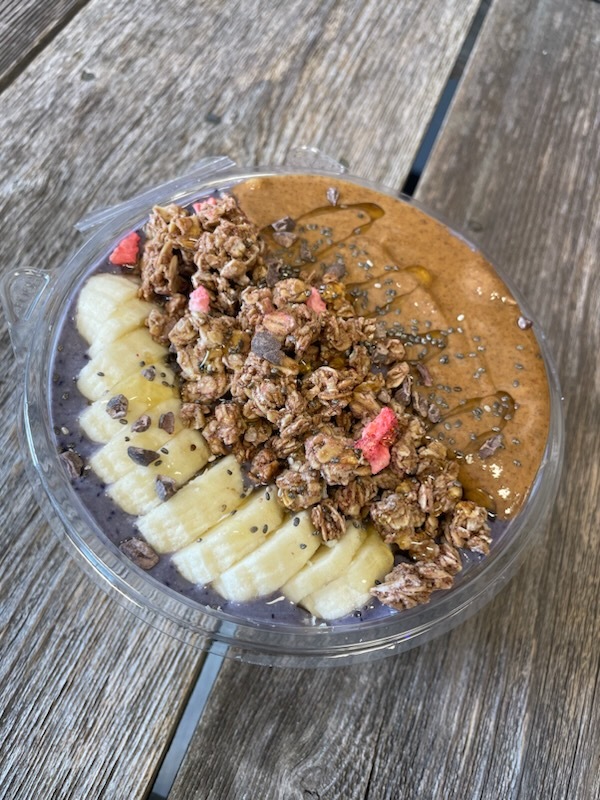 A protein bowl made with banana, granola, and peanut butter. Displayed on a hard wood floor as background.
