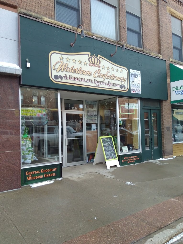 A view of an outside entrance to an sweet shop, brick walls with a green awning with a sign reading "Watertown Confectionery"