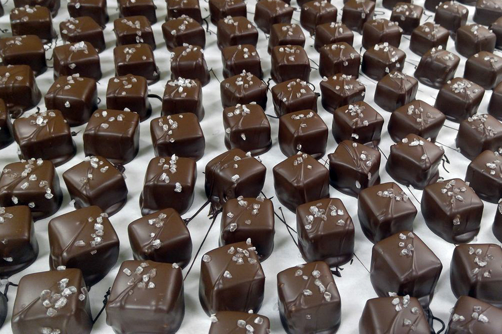 A view of rows of chocolates with chocolate drizzle and sea salt sprinkled on top.