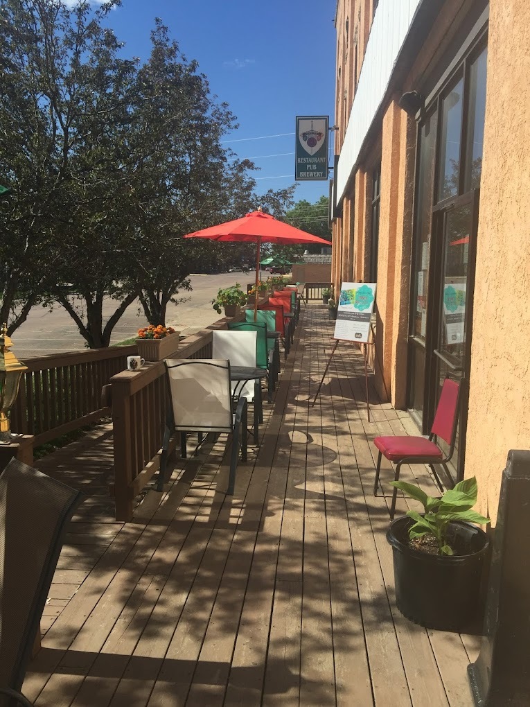 Outside view of an entrance to a pizza shop with seating out front and a red umbrella covering a table.
