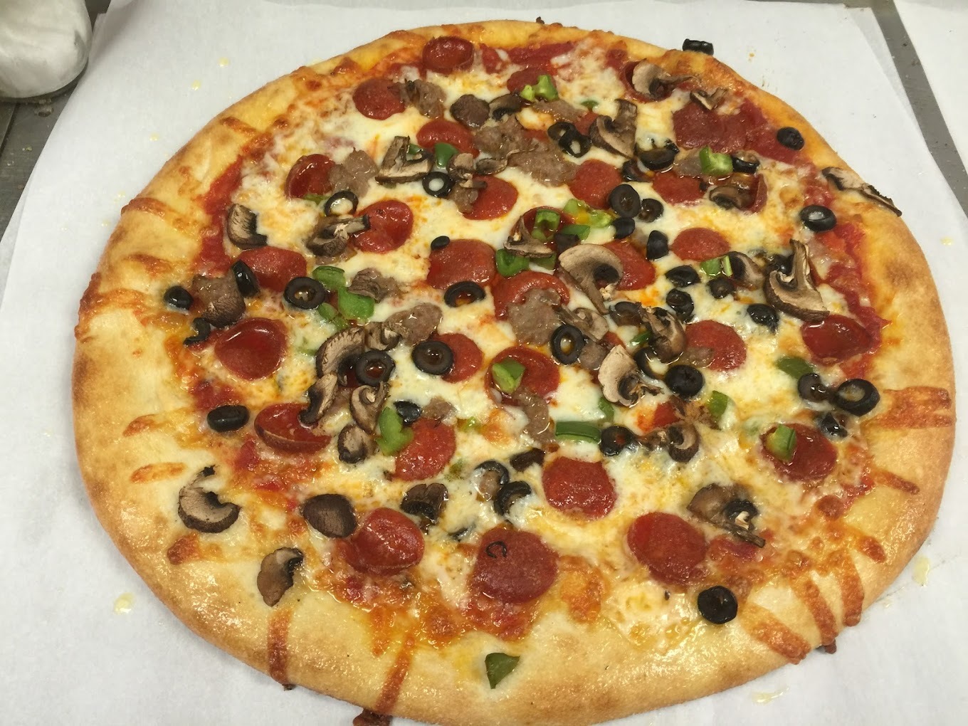 A view of a pizza topped with cheese, pepperoni, olives, and peppers.
