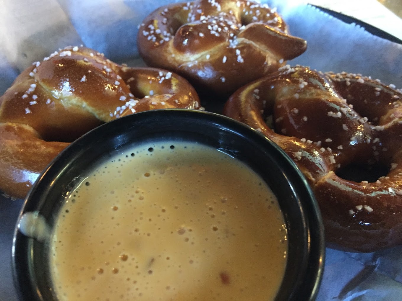 A basket with three large pretzels and a side cup of cheese.