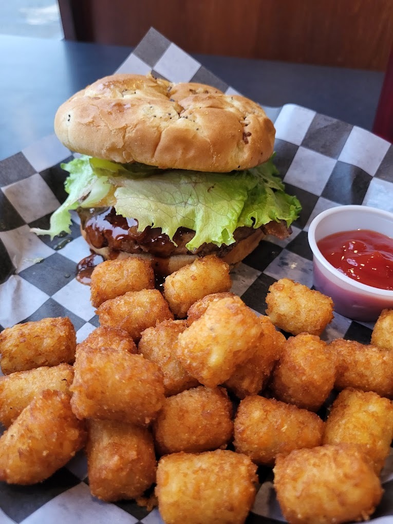 A view of a burger with lettuce and a side of tots and fries.