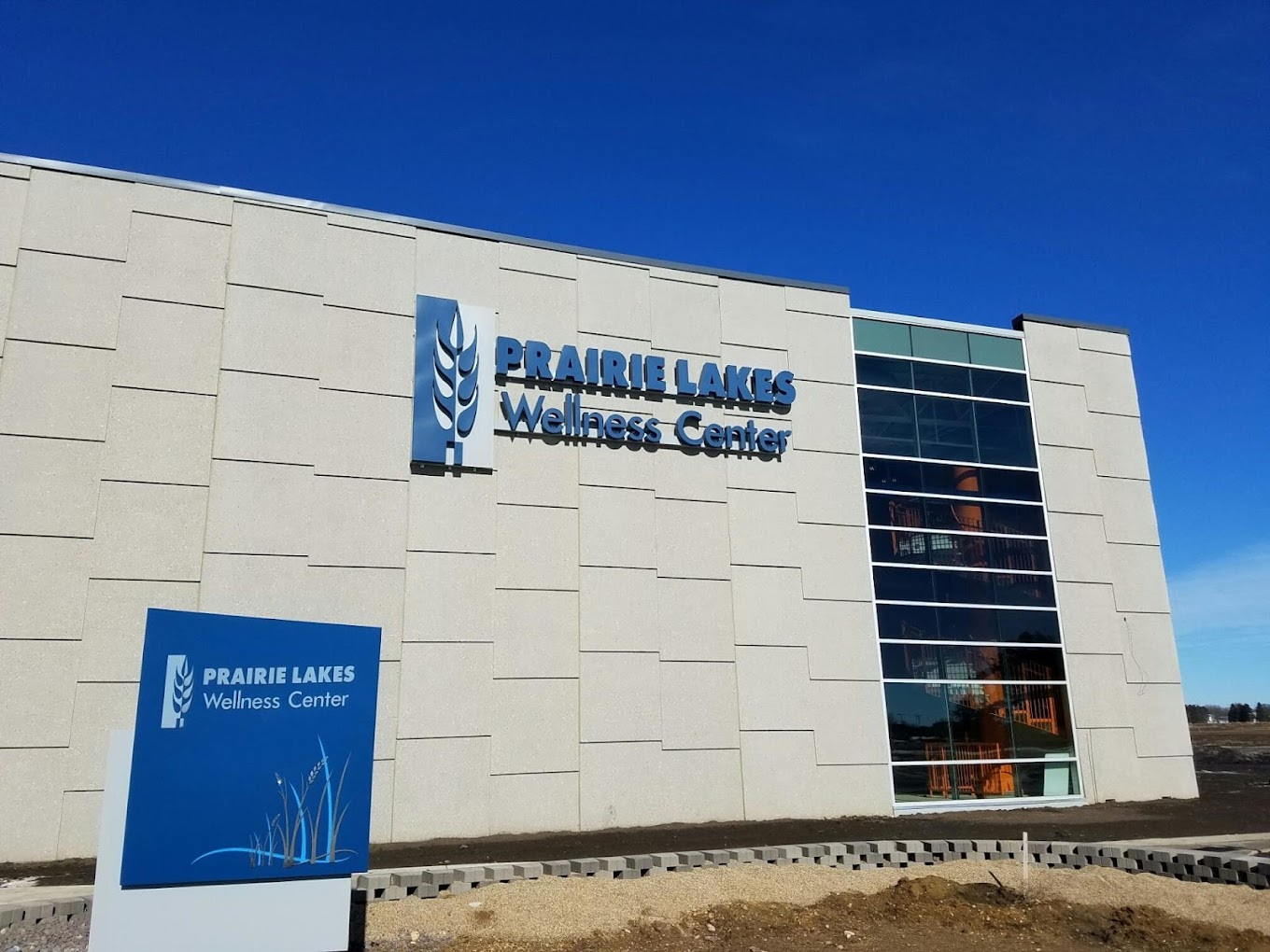 A large grey building with a row of windows on the side, and a sign on the building that reads "Prairie Lakes Wellness Center"