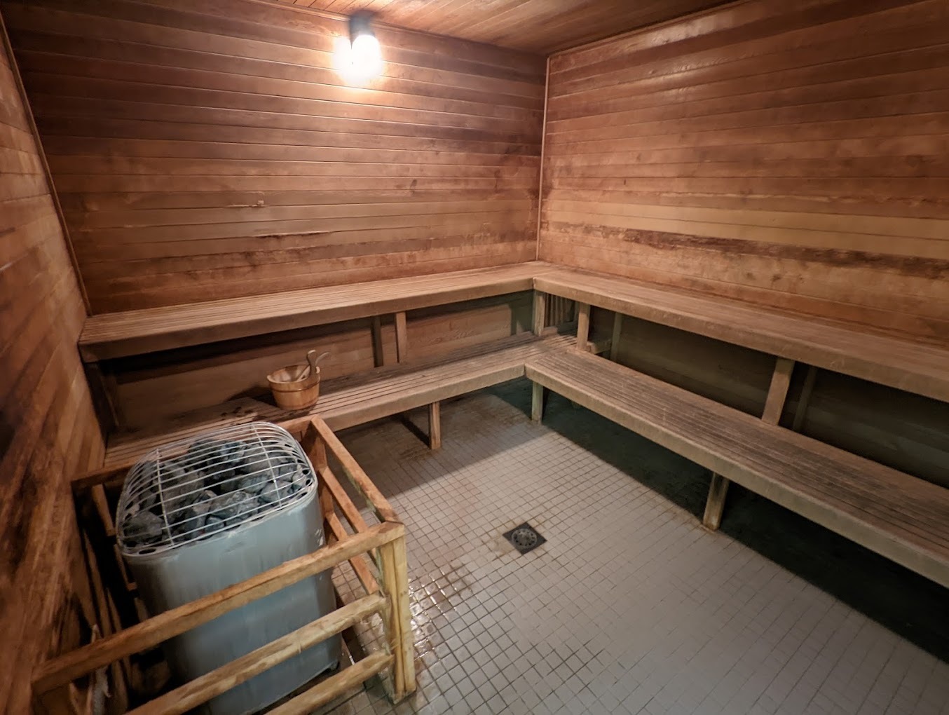 A look into a sauna room, a dimly lit small room with wood paneling and benches lining the walls.