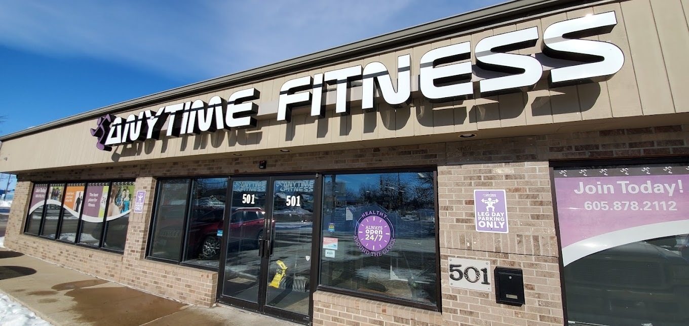 A beige strip mall type building, above the windows and entrance of the gym is a large sign in white lettering reading "Anytime Fitness"
