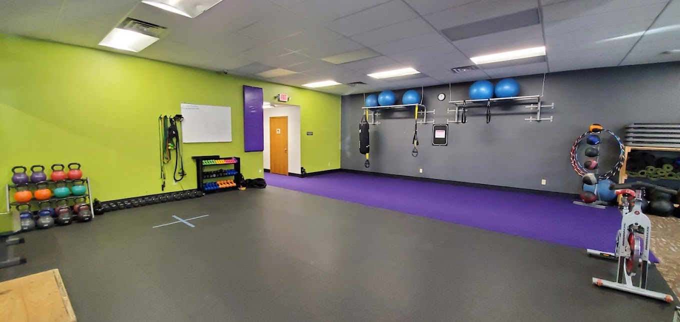 A large room with a green accent wall, and various workout accessories on the wall such as weights, jumping ropes, and exercise balls.