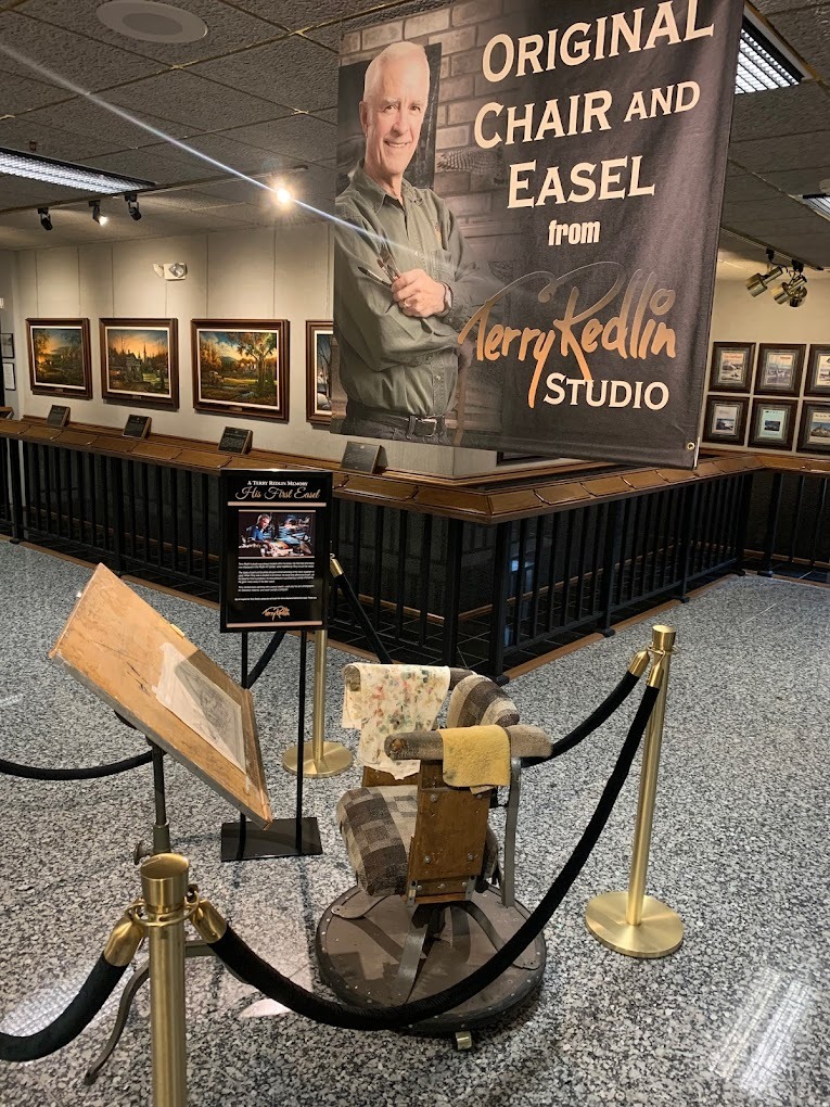 A museum with many pictures along the wall and a chair and easel roped off in the middle of the room.